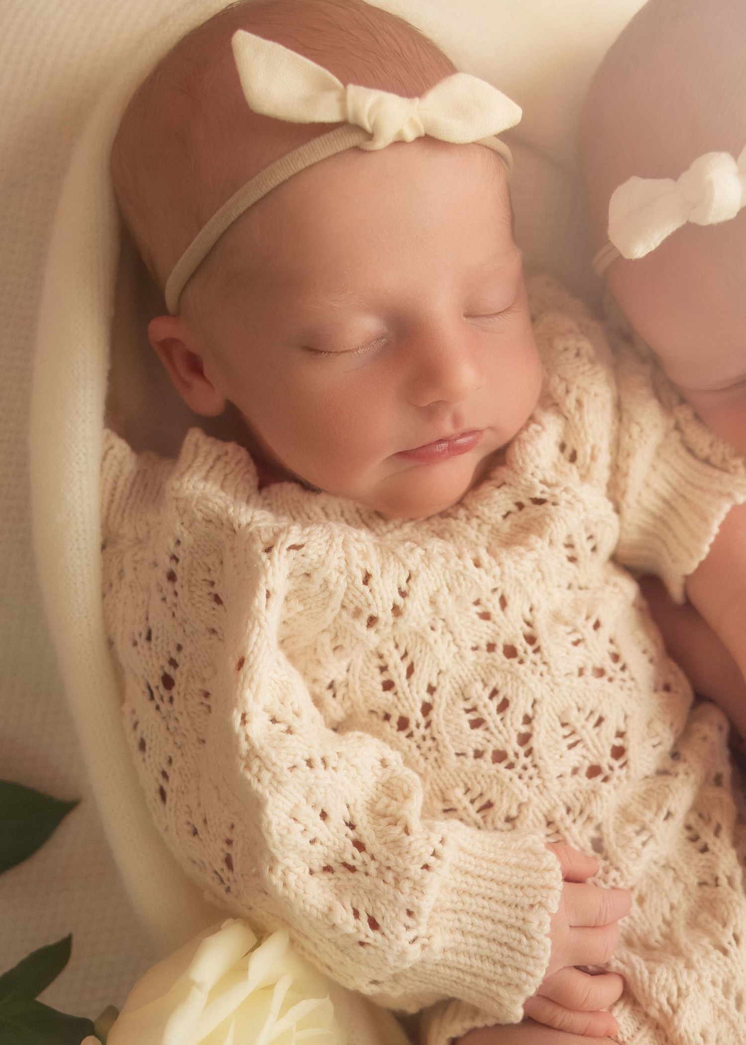 Sleeping newborn twins in cream knit sweaters and white bow headbands, peaceful newborn photography.