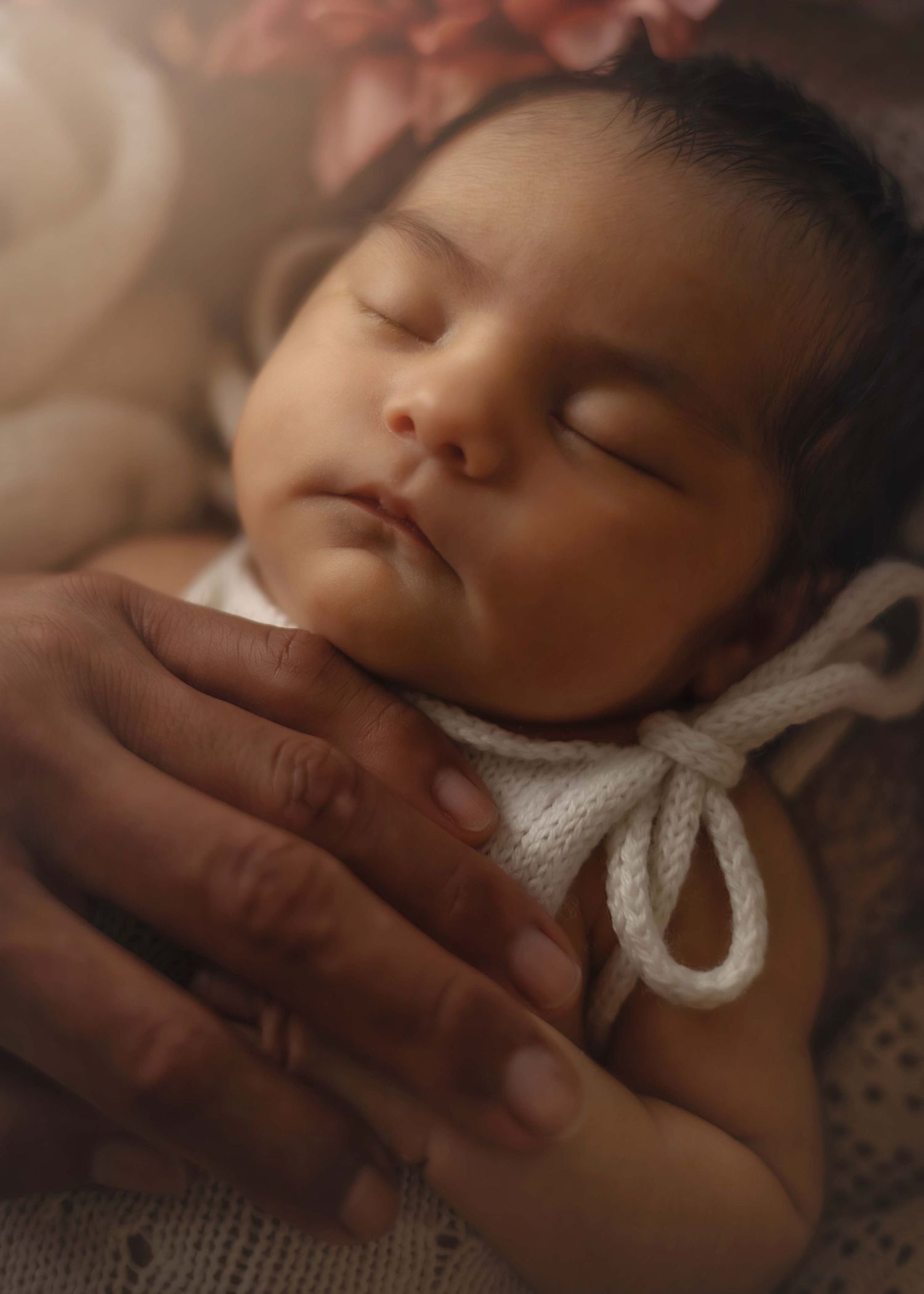 Peaceful sleeping newborn baby cradled in loving adult hands, wearing a white knit outfit with bow tie.