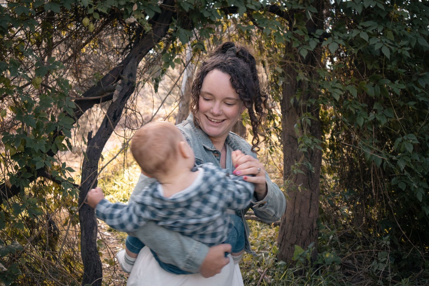 Outdoor family photography of mother holding baby under trees in natural light
