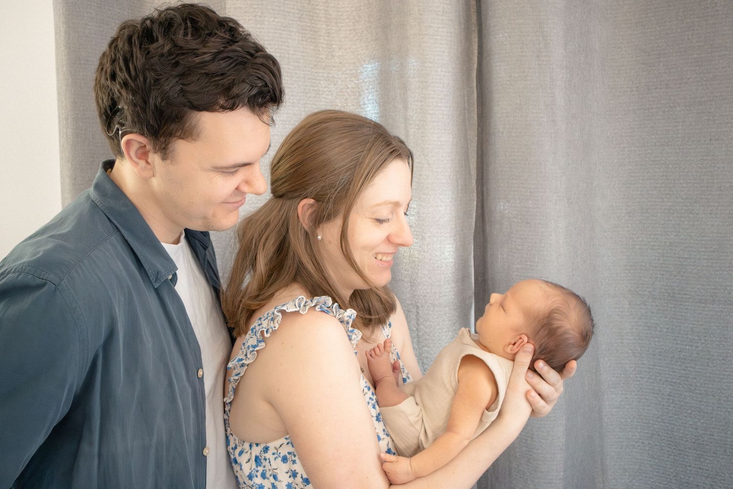 In-home newborn session with parents admiring baby in soft window light