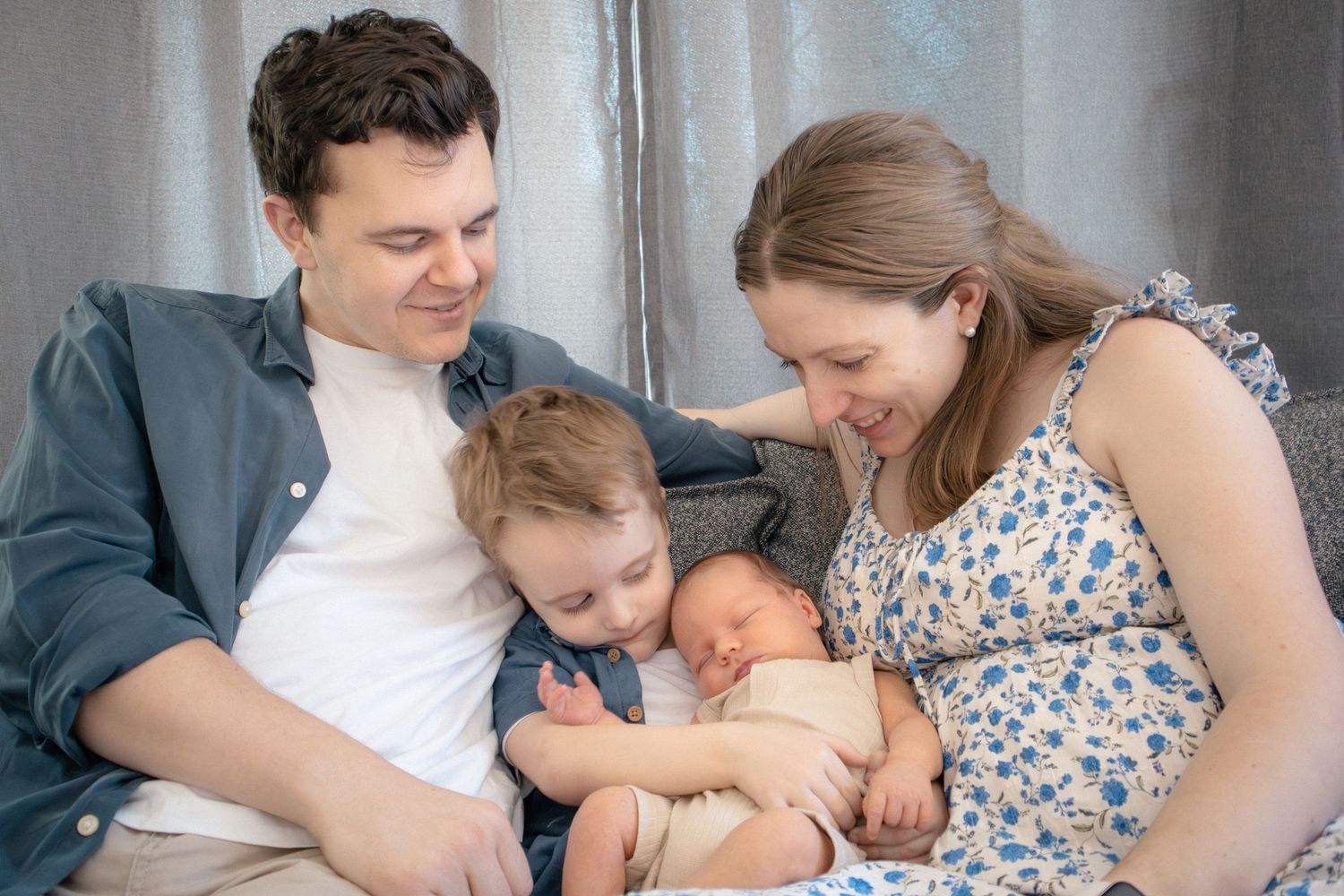 In-home newborn photography of family cuddling newborn on couch in soft natural light