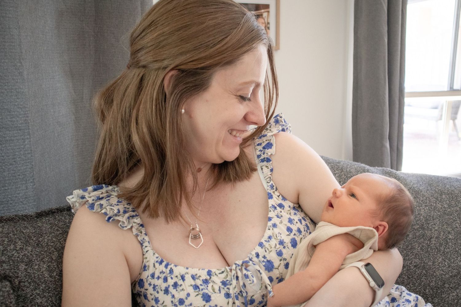 Mother holding newborn and smiling during natural in-home session