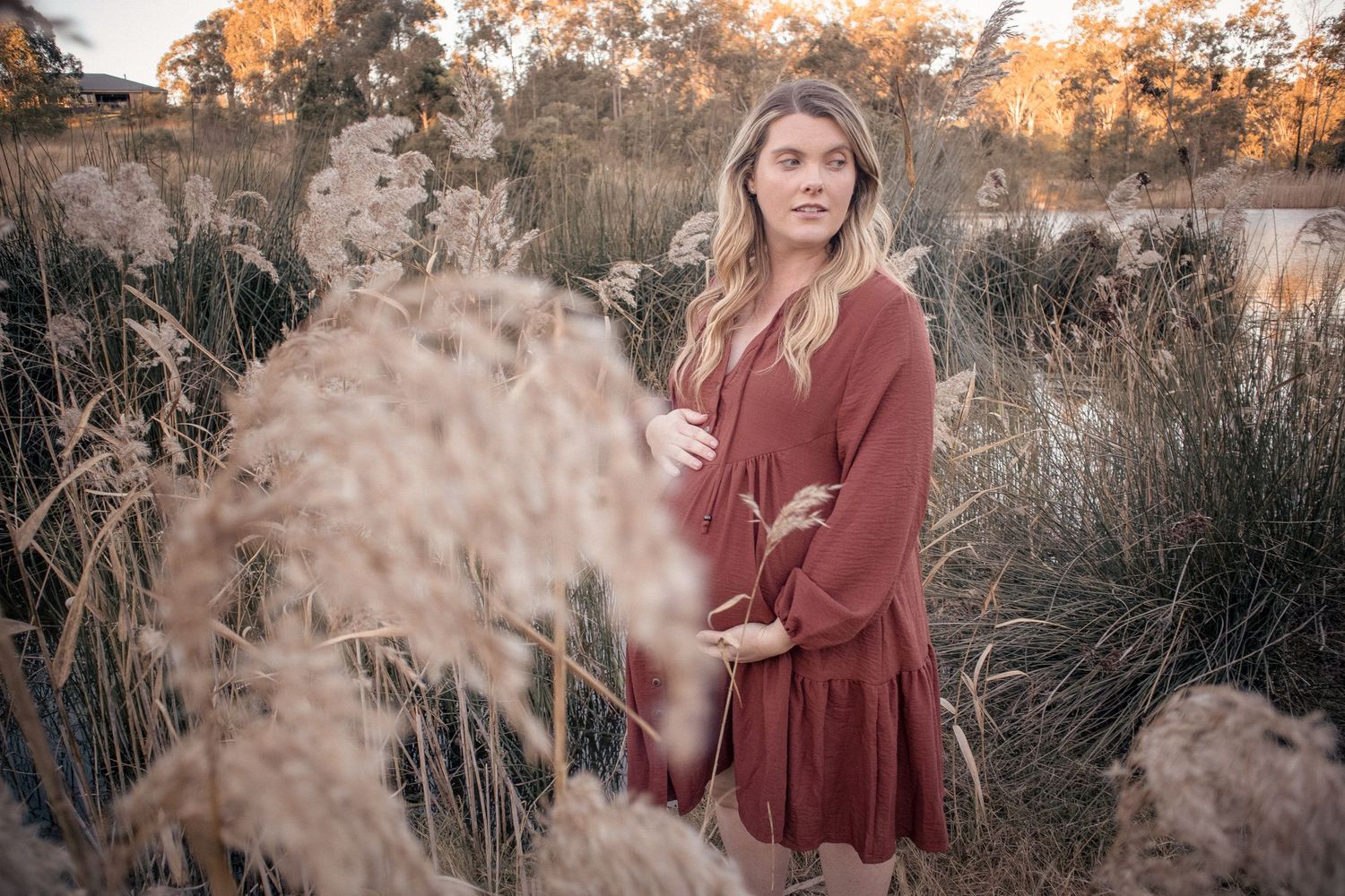 Natural maternity photography of pregnant mother standing among tall grass at sunset