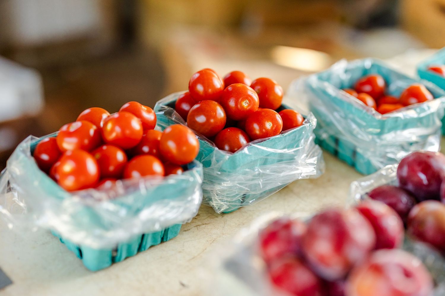 Fresh cherry tomatoes displayed in blue baskets at a market stand.