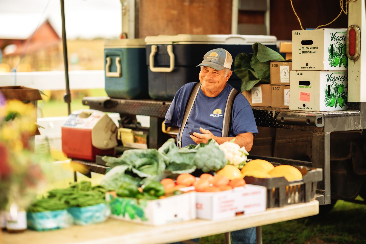 Vendor arranging fresh produce at an outdoor farmers market stand.