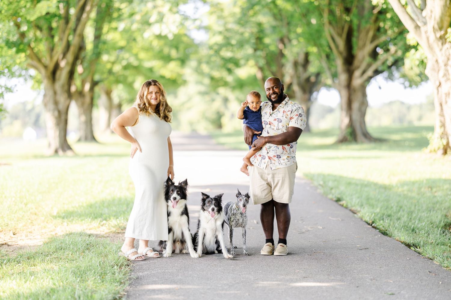 Family and pets posing together on a scenic walking trail surrounded by trees.
