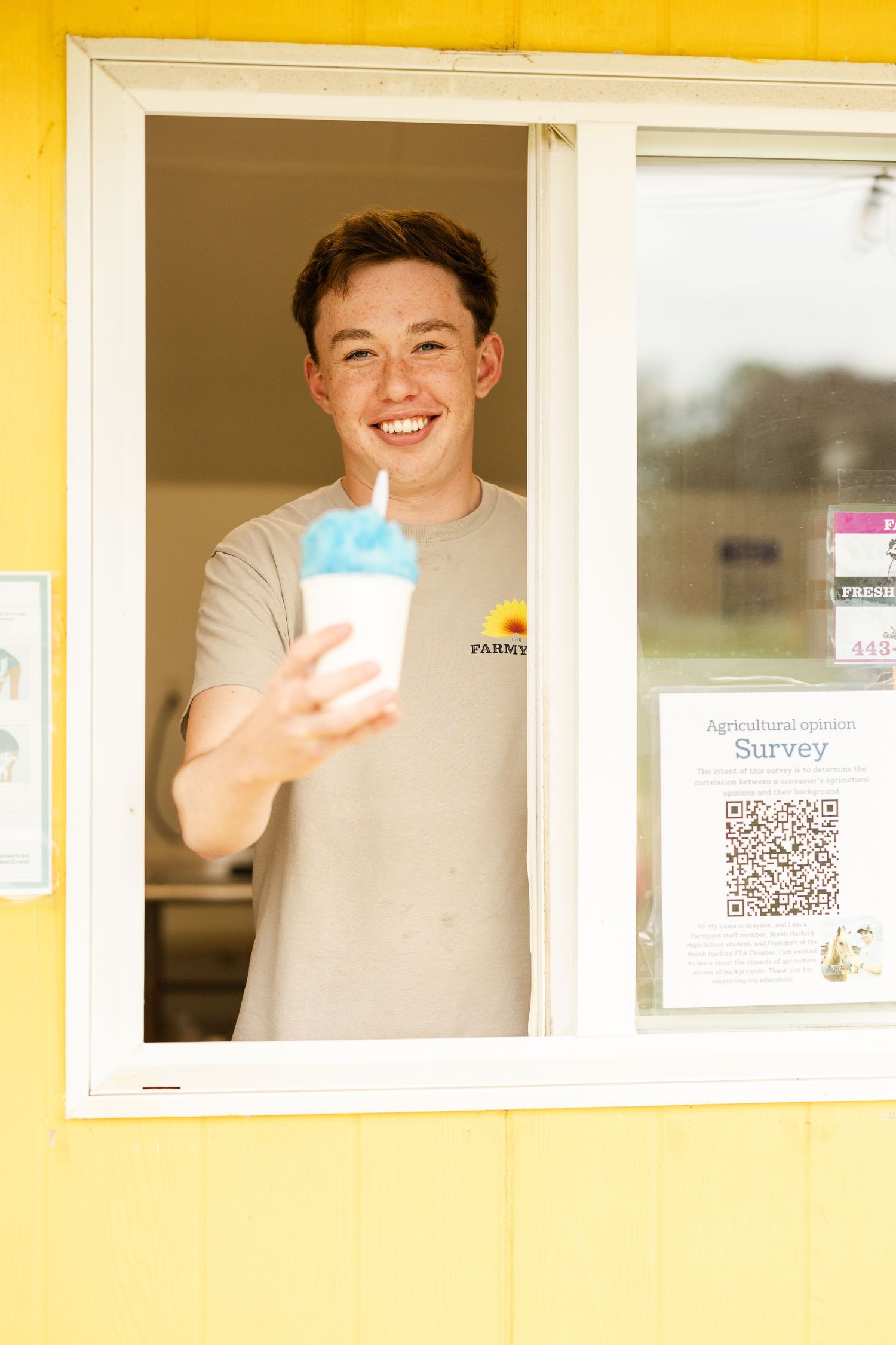 Employee serving drinks through a yellow-framed service window.