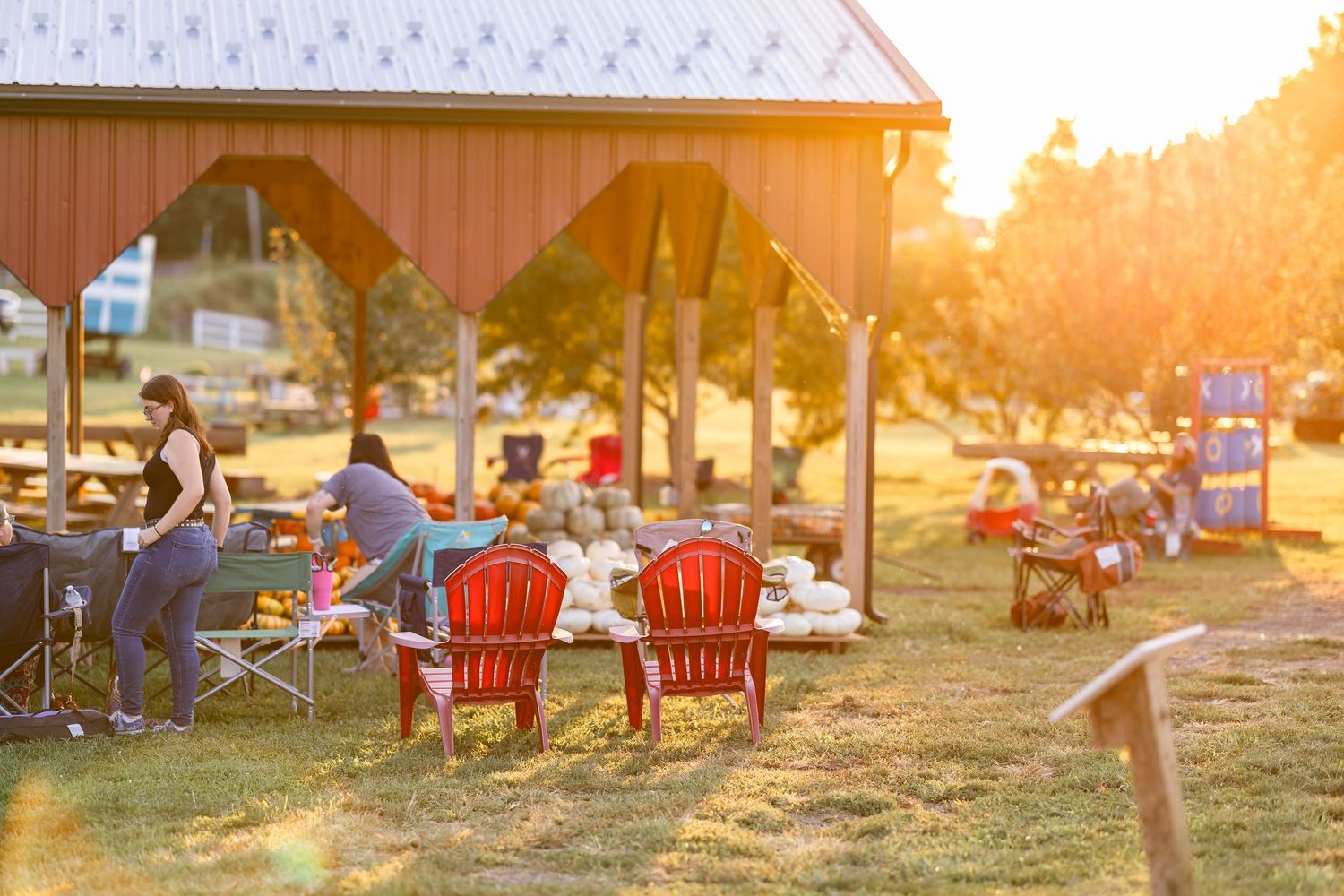 People relaxing in red Adirondack chairs at an outdoor gathering during sunset.