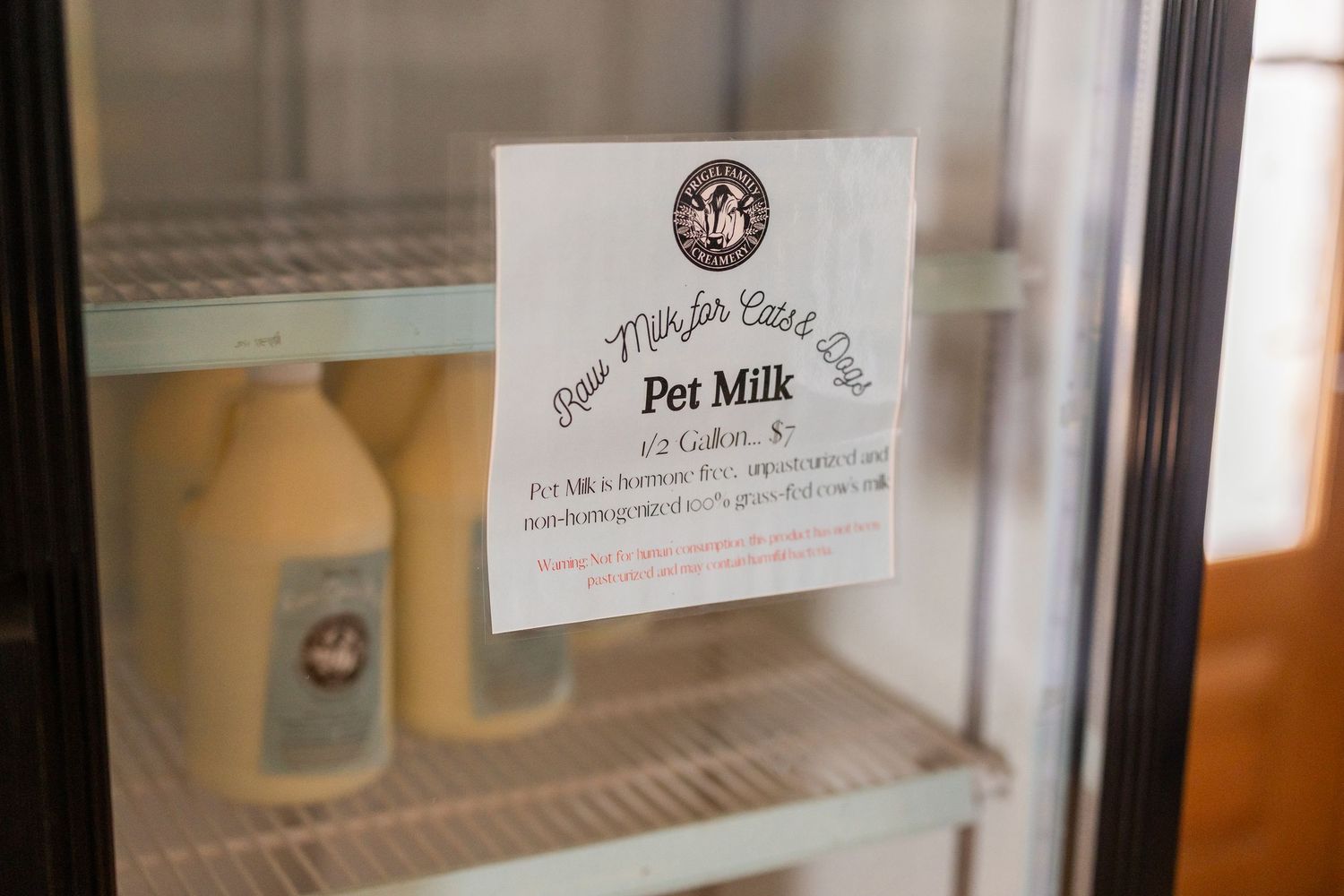 Refrigerator display case with glass door showing Pet Milk bottles and a handwritten sign inside a store.