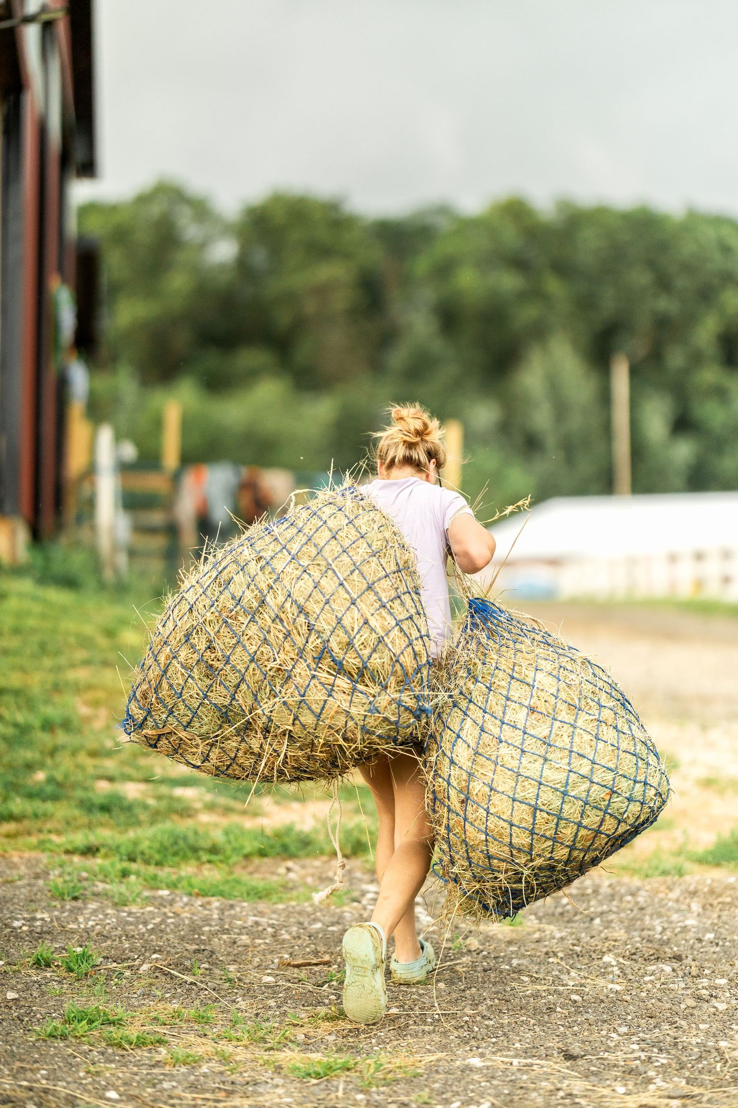 Person carrying large hay bale nets across a farm field.