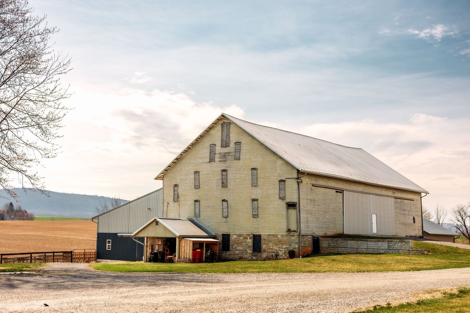 Large traditional white barn with metal roof stands against cloudy rural landscape.