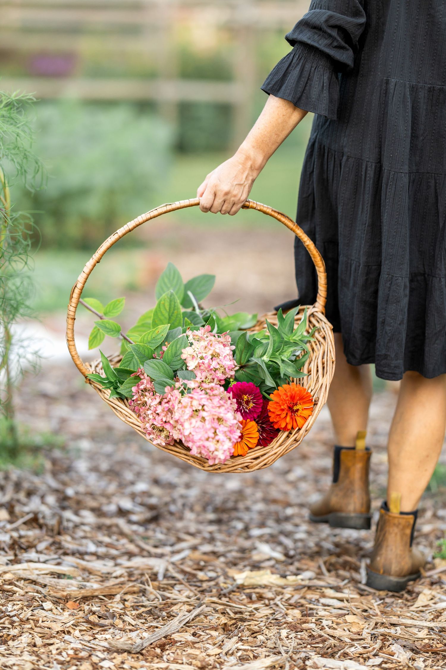 A wicker basket filled with colorful flowers and produce swings through a garden.