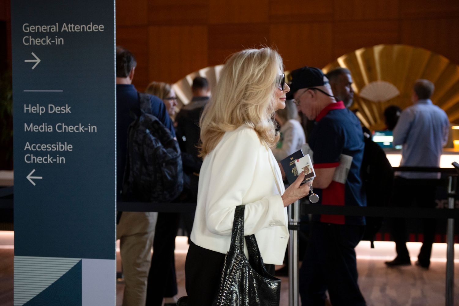 Attendees line up at a conference check-in area with directional signage for general, media, and accessible registration.