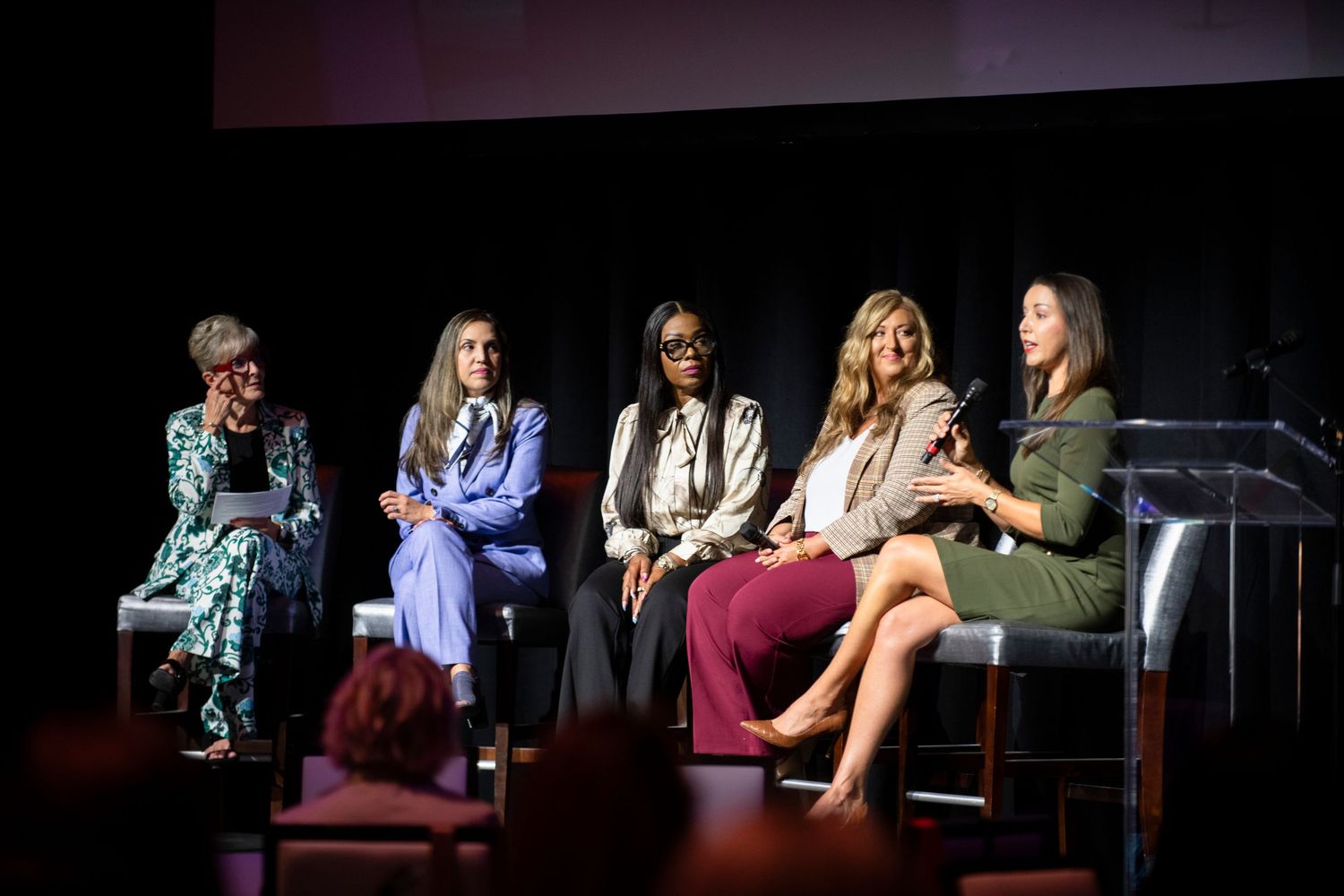 Five women seated on stage during a panel discussion at a professional conference event.