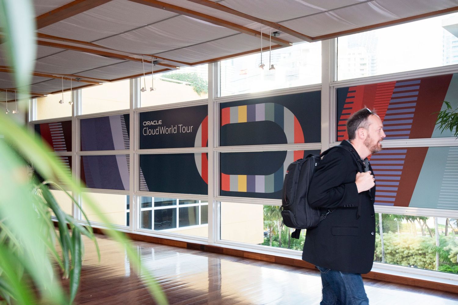 Man with backpack walking past Oracle CloudWorld Tour banner display in modern building interior.