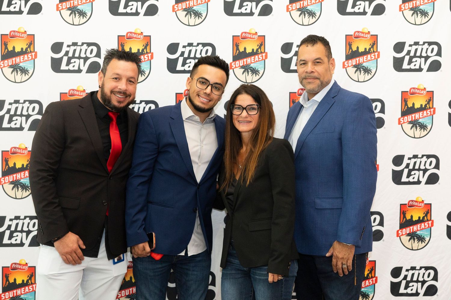 Four people posing together at a Frito-Lay branded event backdrop, smiling for a group photo.