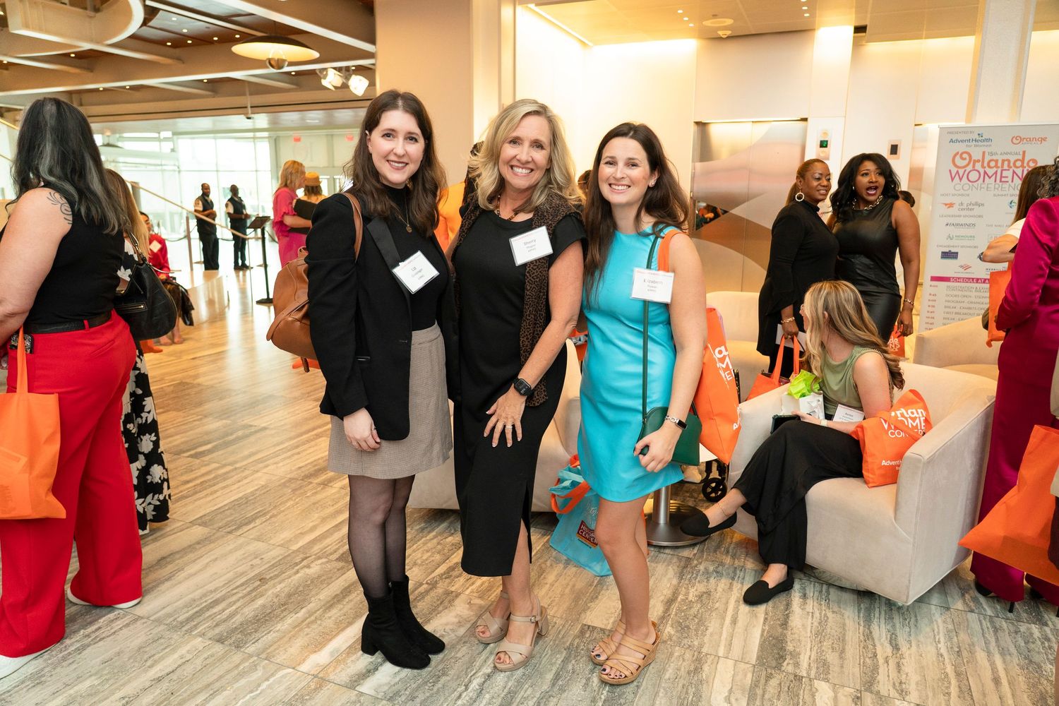 Three women smiling and posing together at a professional networking event in a modern office space.