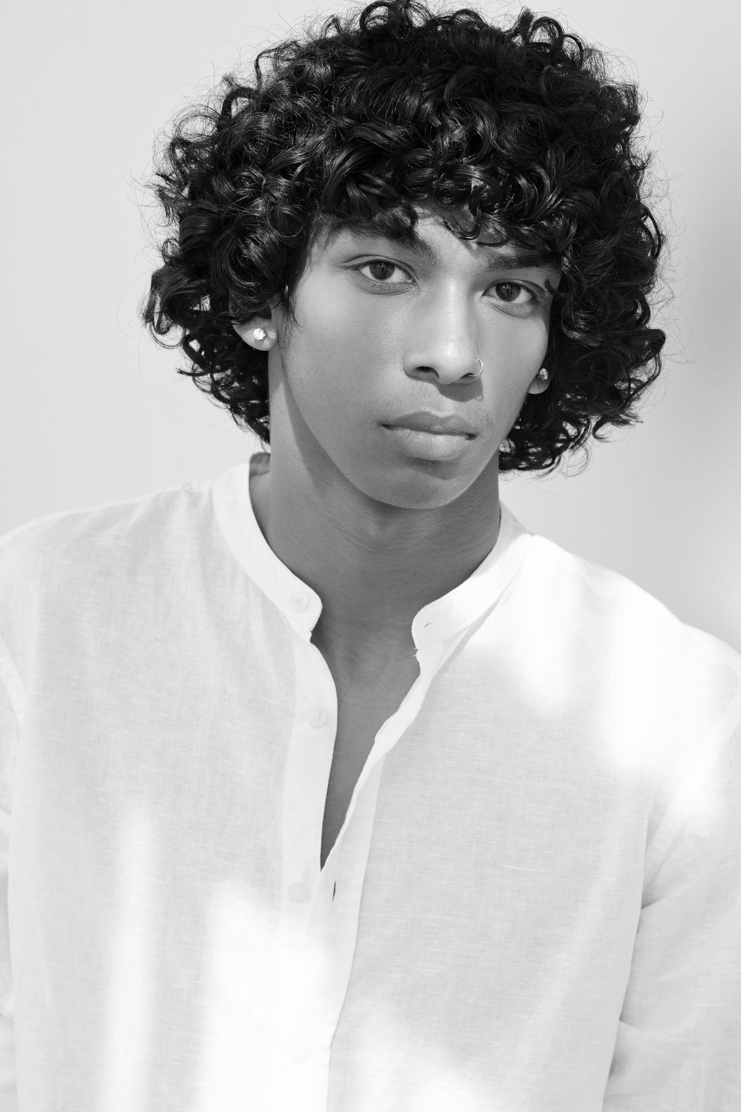 Black and white portrait of a young man with curly hair wearing a white linen shirt.