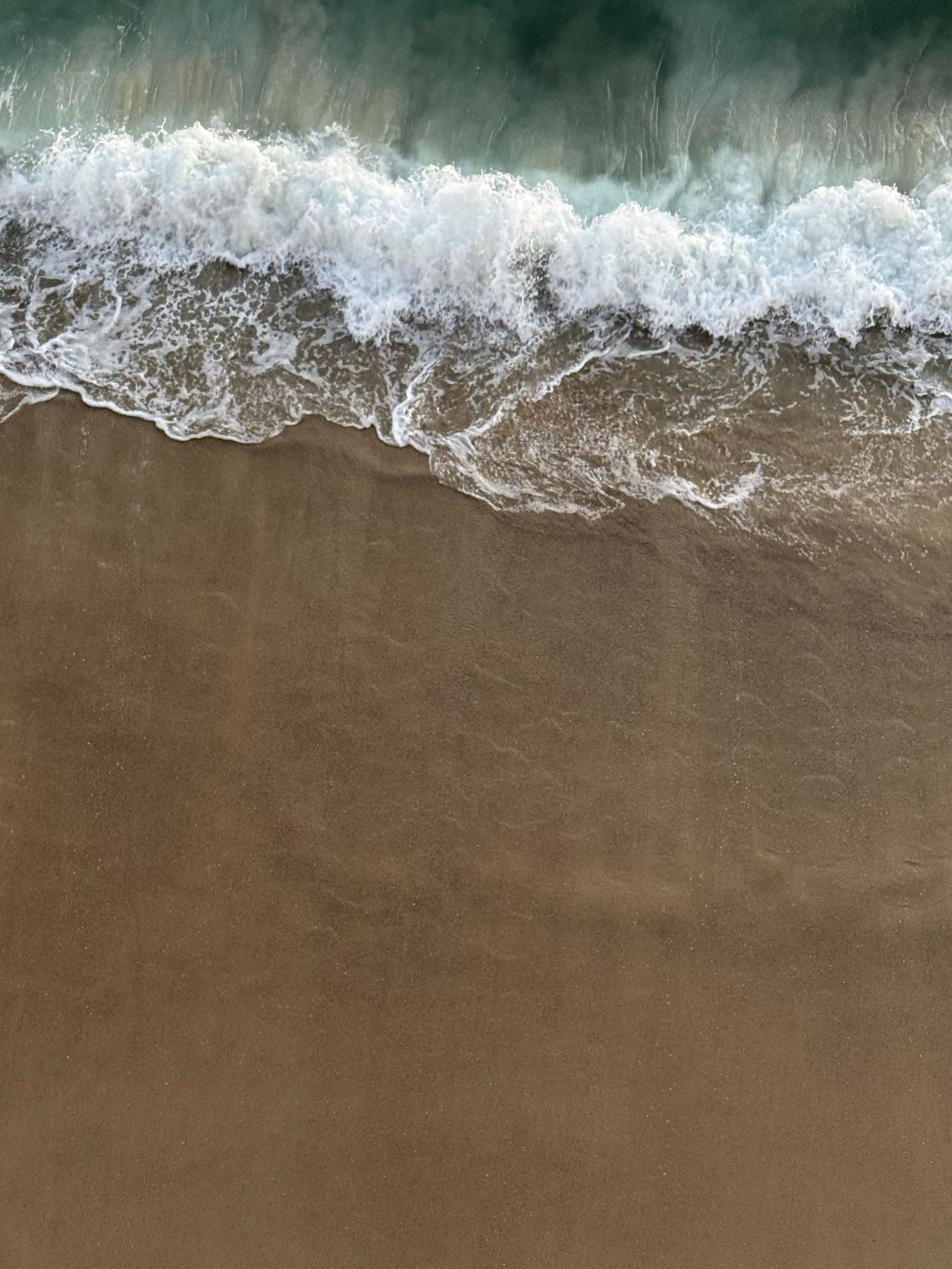 Aerial view of ocean waves washing onto sandy beach shoreline from above.