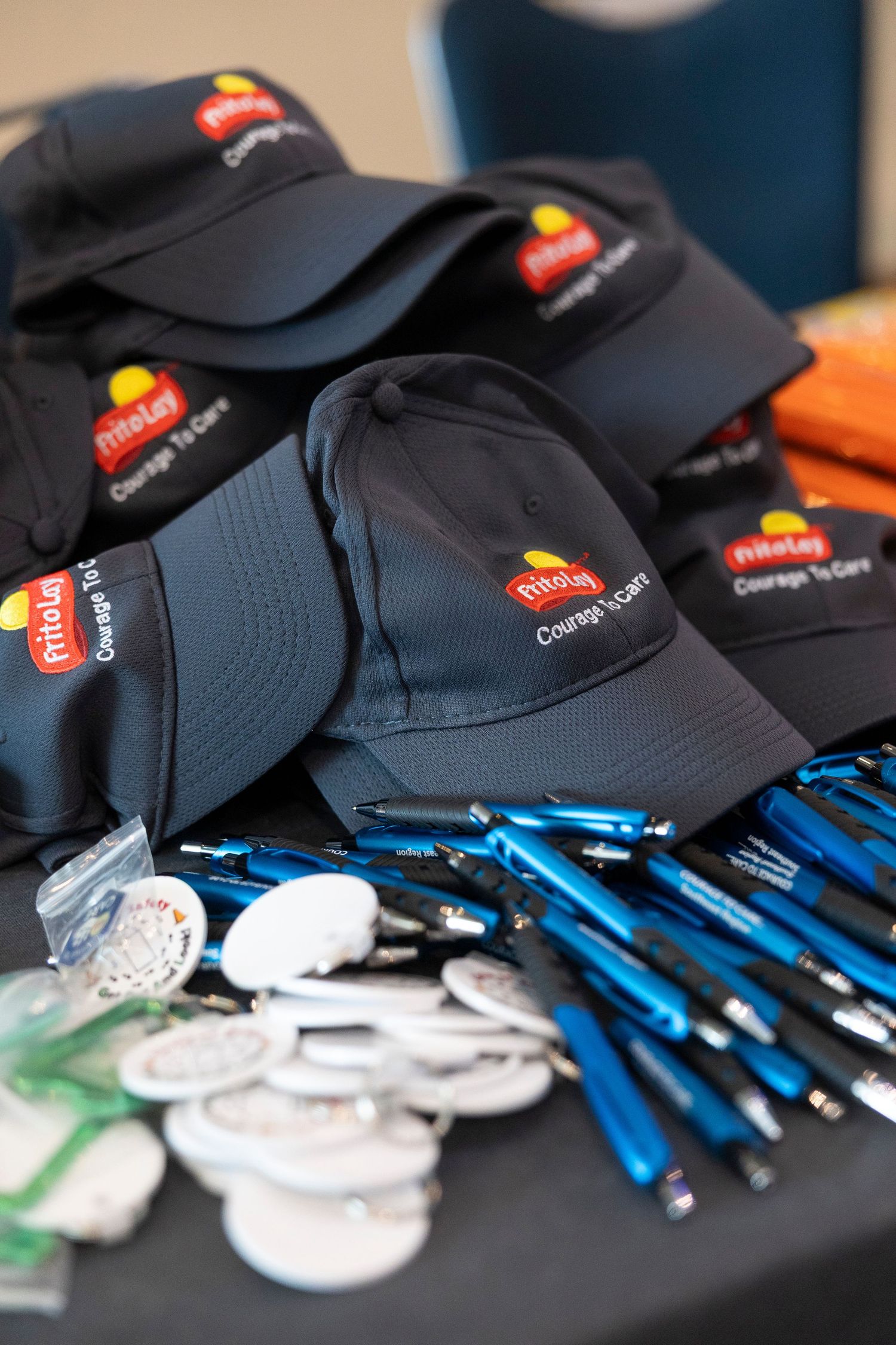 Frito-Lay branded merchandise including navy caps, blue pens, and white buttons displayed on a table at a corporate event.