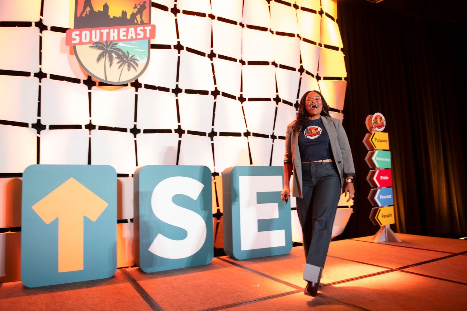 Woman posing on stage at Southeast conference with large TSE letters and arrow prop decorations.