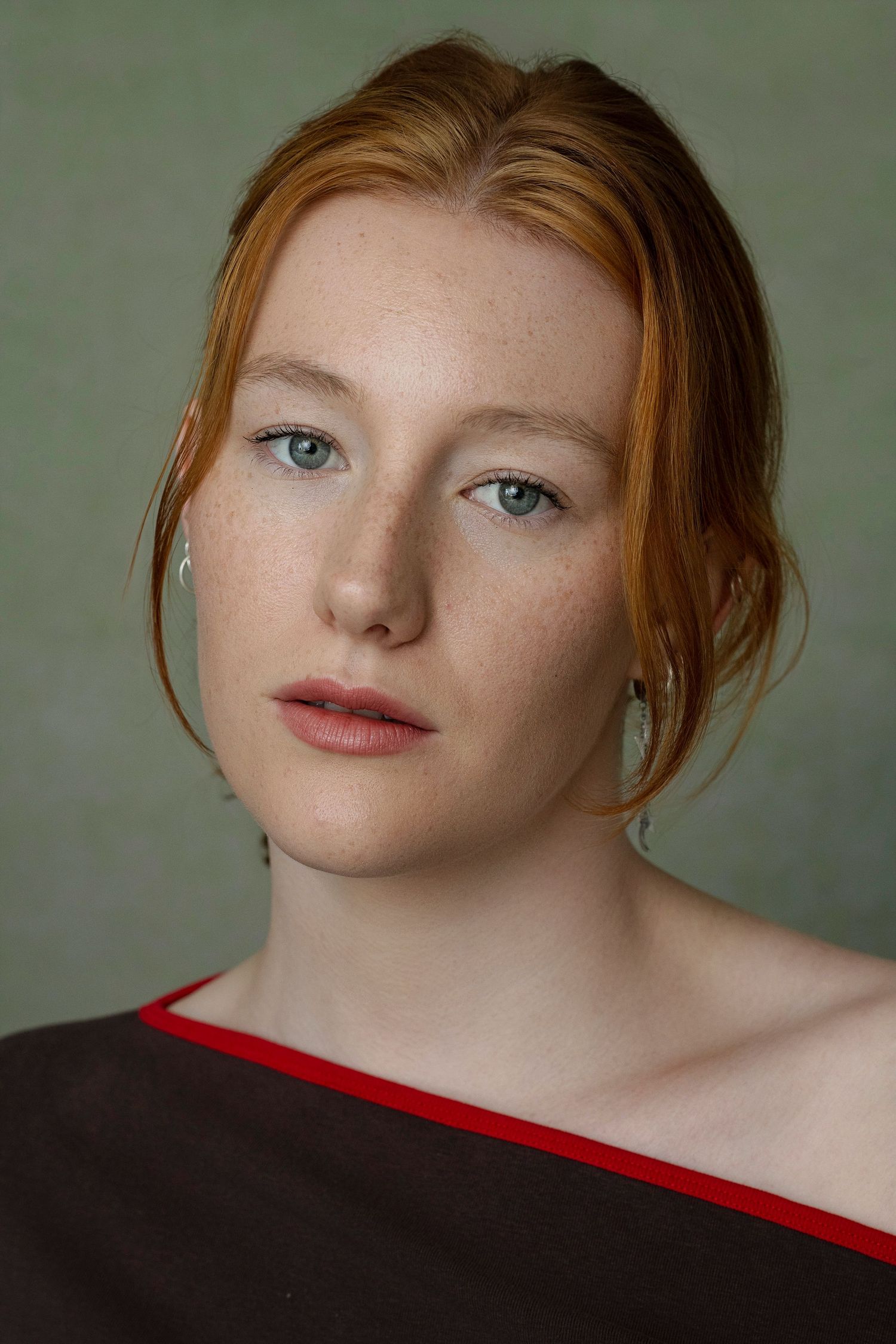 Portrait of a young redhead woman with freckles wearing a dark off-shoulder top.