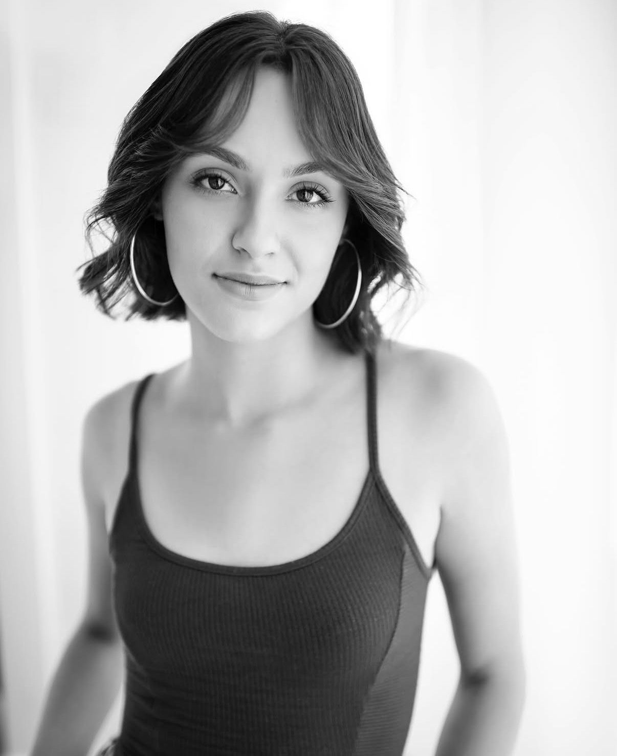 Young woman with bob haircut in black tank top smiling in black and white headshot.