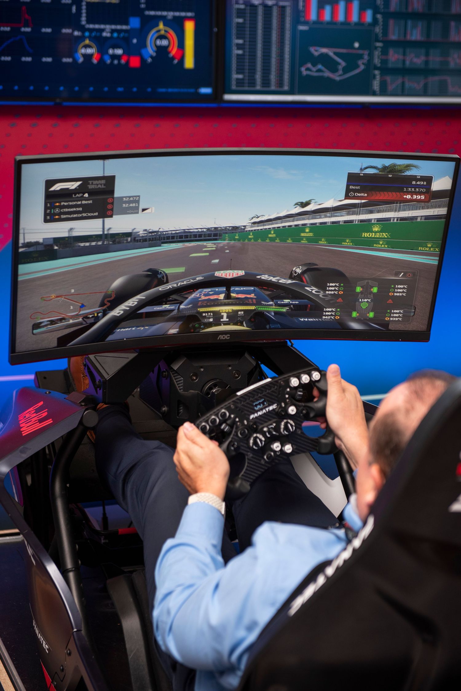 Person using an F1 racing simulator with a large curved monitor displaying a Formula 1 video game cockpit view.