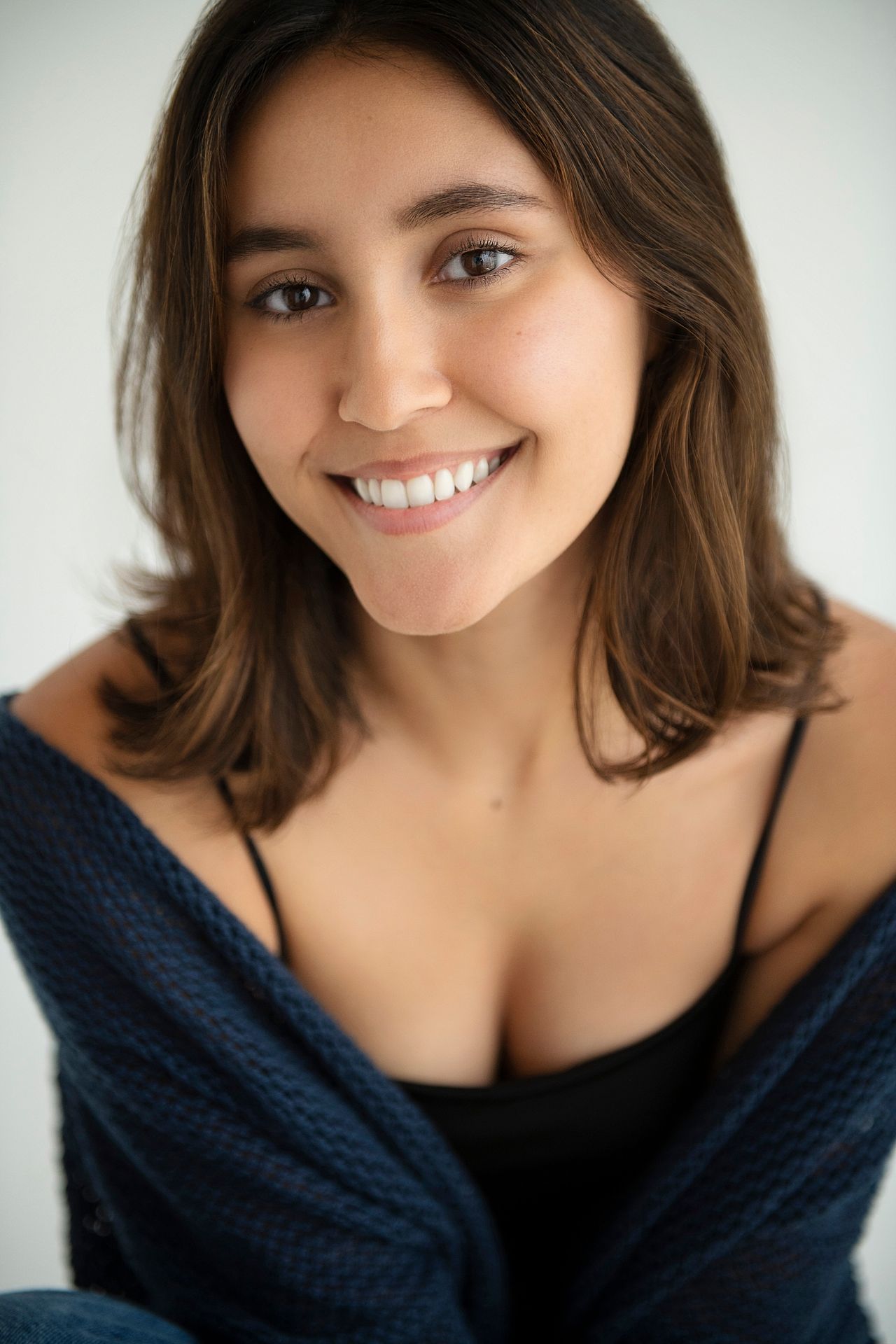 Smiling young woman with brown hair wearing a navy cardigan and black top in a studio portrait.