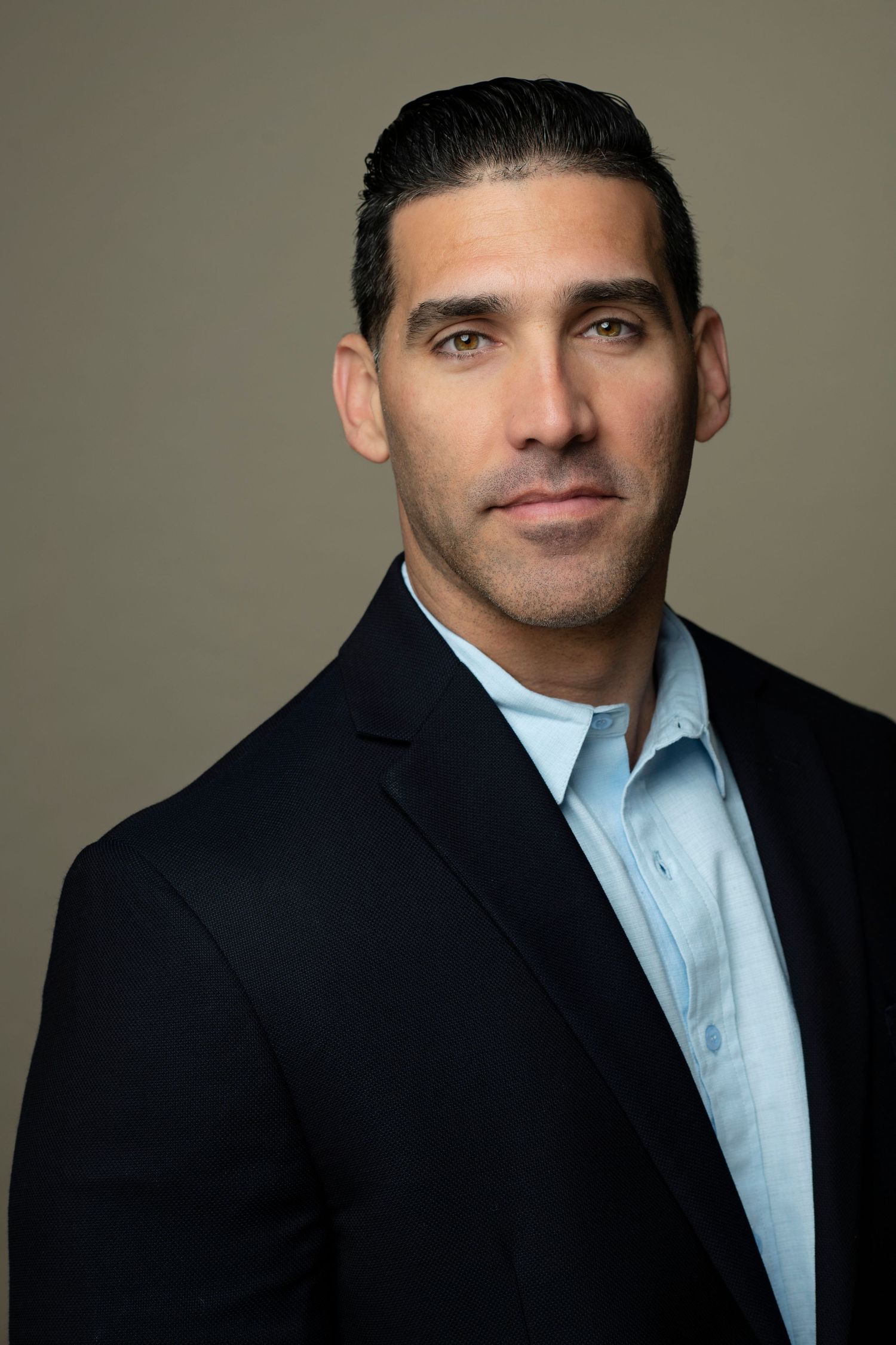 Professional headshot of a man in a dark blazer and light blue shirt against a neutral background.