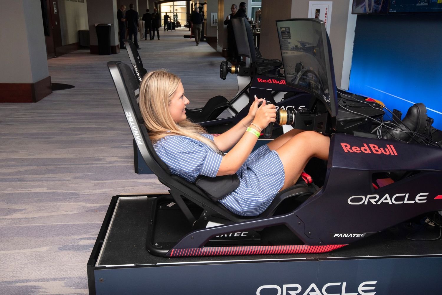 Blonde woman enjoying an Oracle Red Bull Racing F1 simulator at an indoor event.