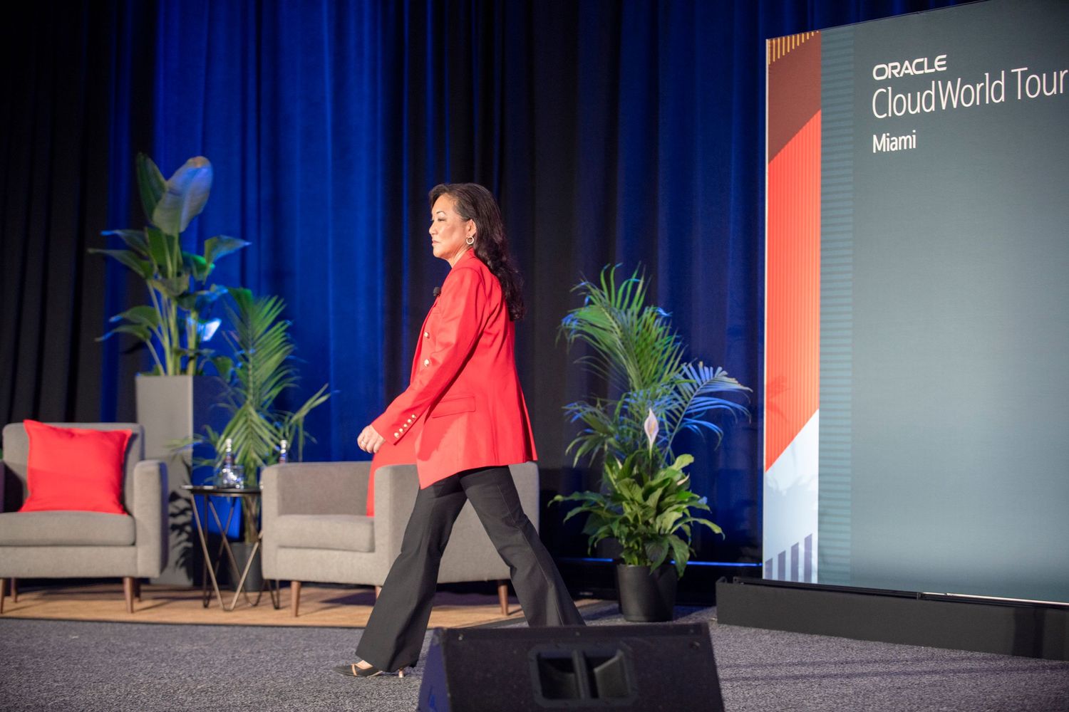 A presenter in a red blazer walks across the stage at Oracle Cloud World Tour Miami event.