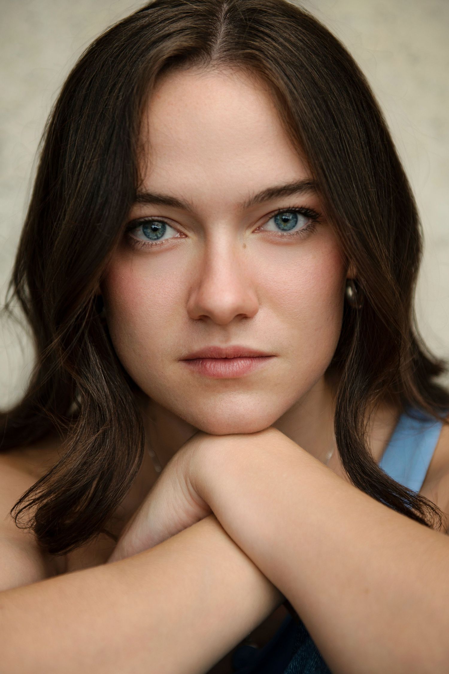 Close-up portrait of young brunette woman with blue eyes resting chin on crossed arms.