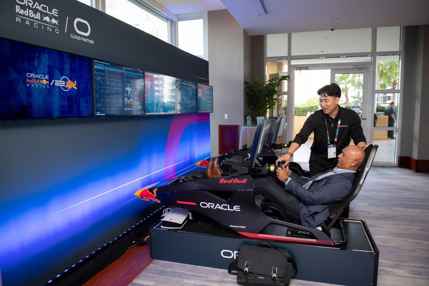 Person trying an Oracle Red Bull Racing F1 simulator setup at an interactive display booth with large screens.