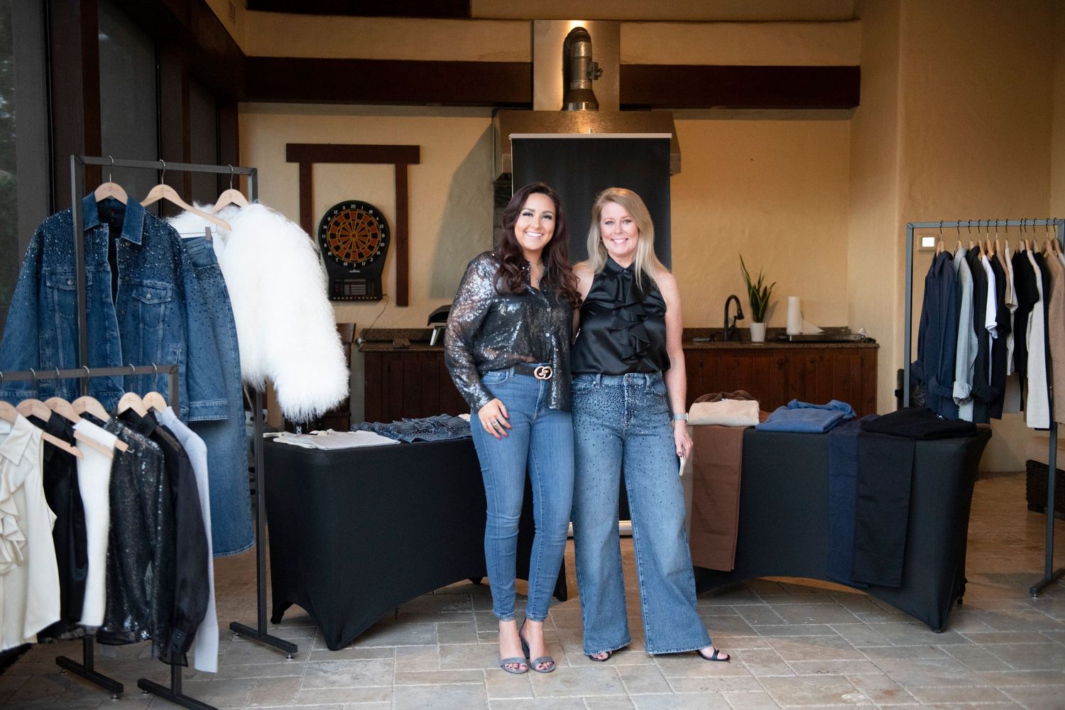 Two women pose together in a boutique clothing store surrounded by denim jackets and stylish apparel displays.