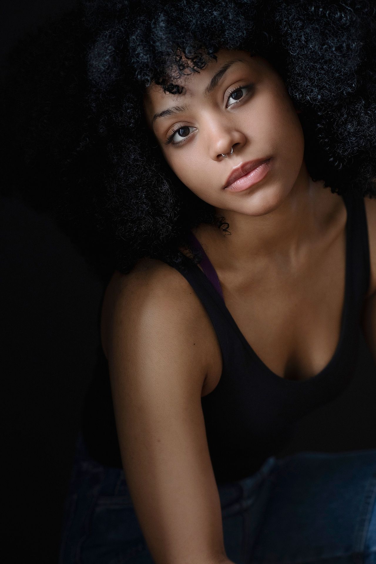 Young Black woman with a large afro hairstyle wearing a black tank top against a dark background.
