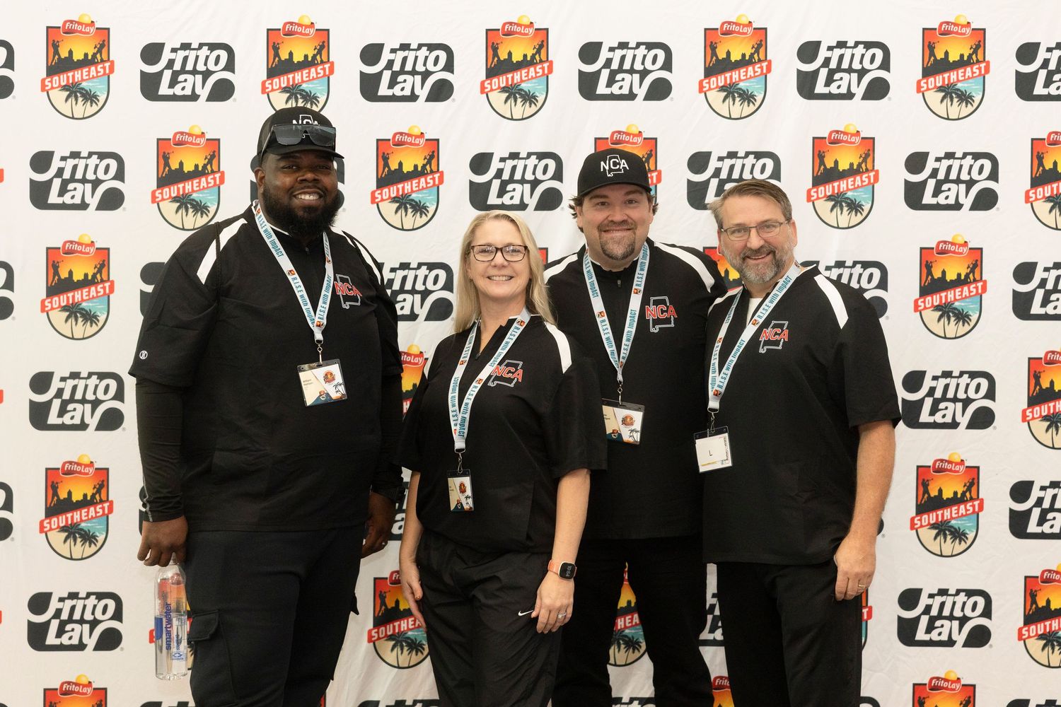 Four smiling employees in black uniforms pose together in front of a Frito-Lay branded step-and-repeat backdrop.