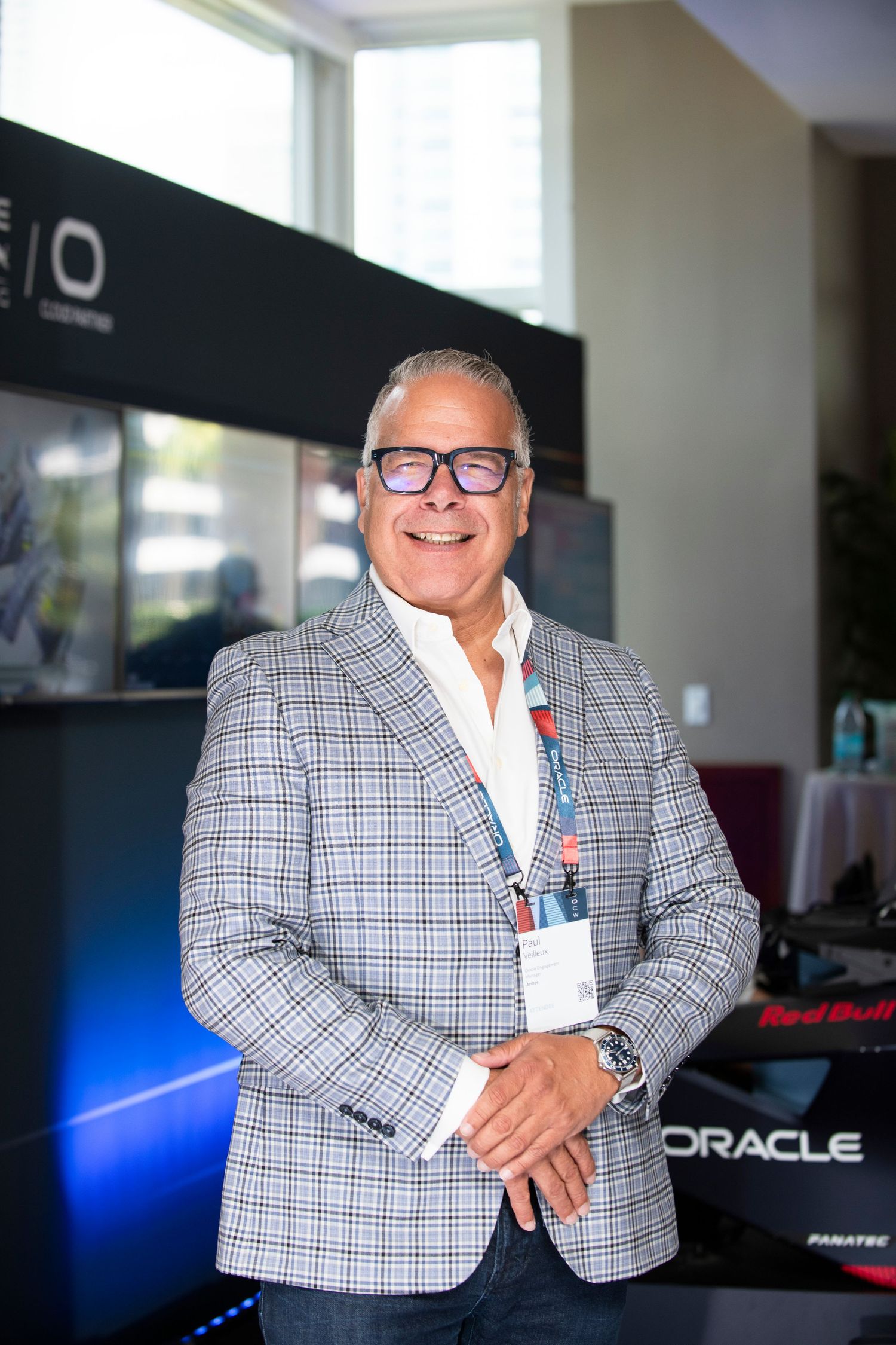 Smiling man in plaid blazer standing at an Oracle Red Bull Racing Formula 1 display.