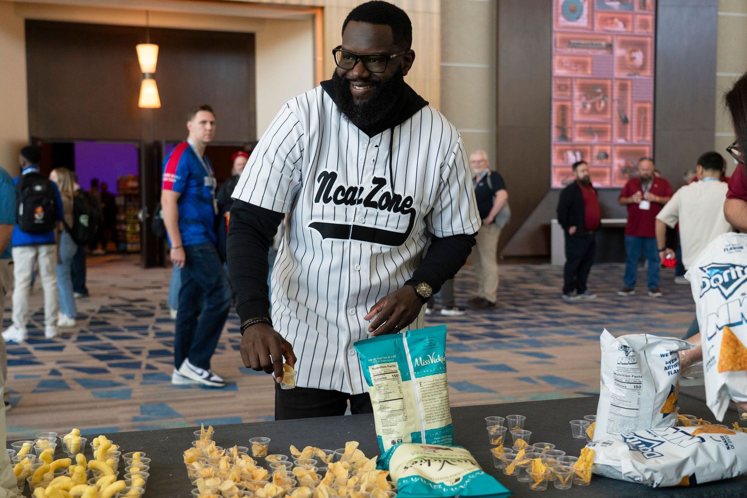 Man in NeatZone jersey arranging snacks at an indoor event table with popcorn and packaged goods.