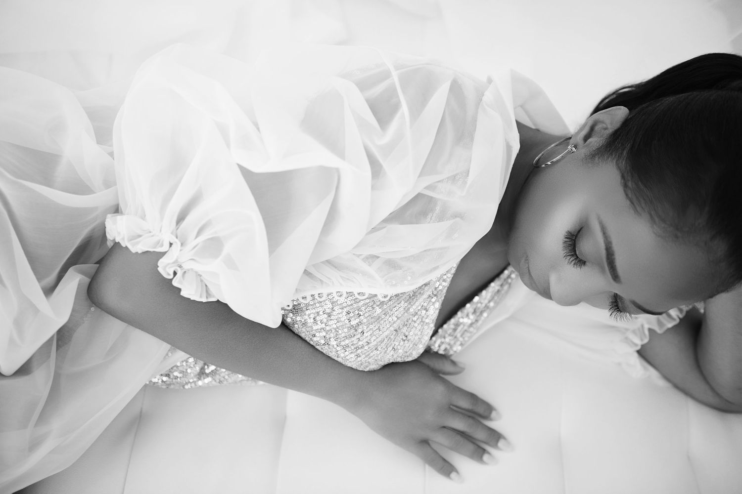 Black and white photo of a young girl in a white lace and tulle dress, looking down gracefully.