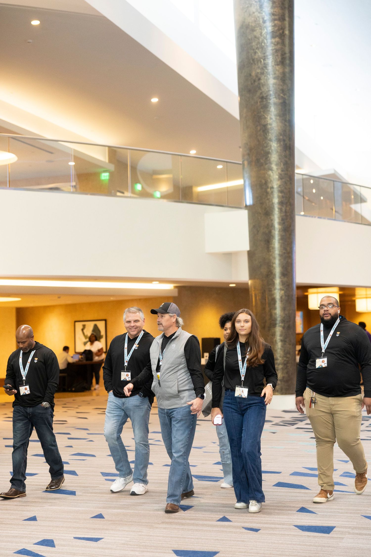 Group of conference attendees wearing lanyards walking through a modern hotel lobby atrium.