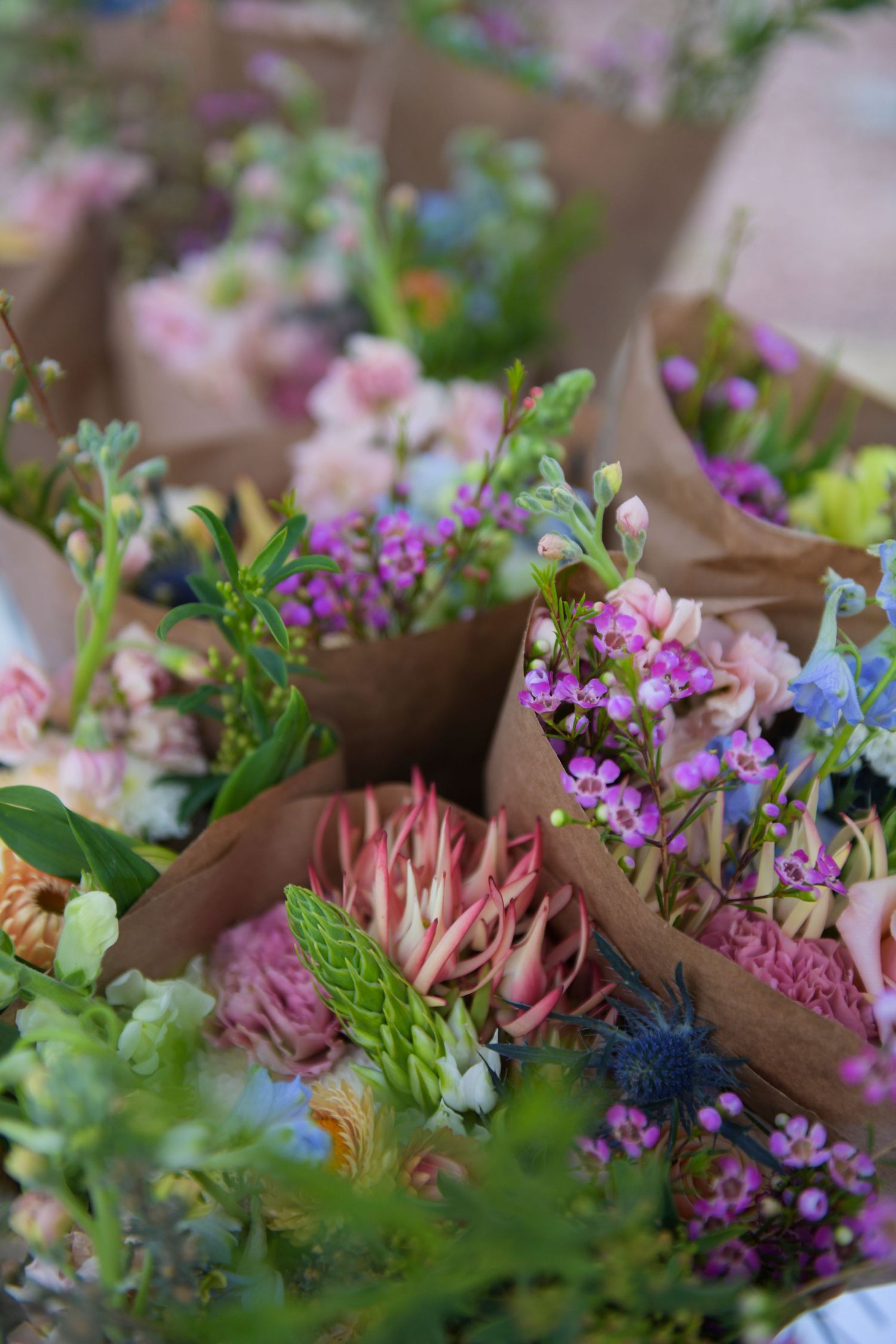 Colorful fresh flower bouquets wrapped in brown kraft paper at a market, featuring pink, purple, and blue blooms.