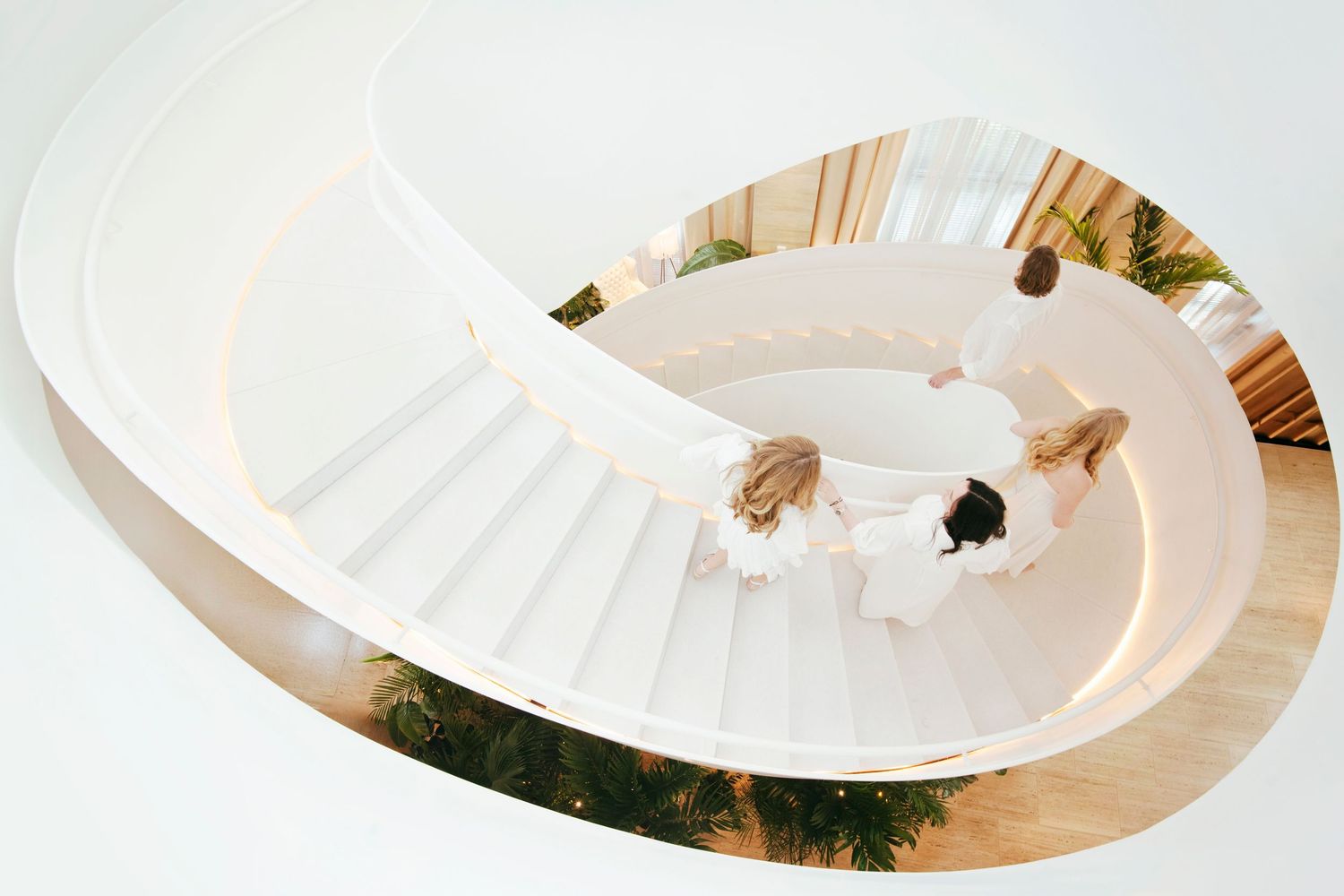 Aerial view of two people descending a modern white spiral staircase with wood flooring.