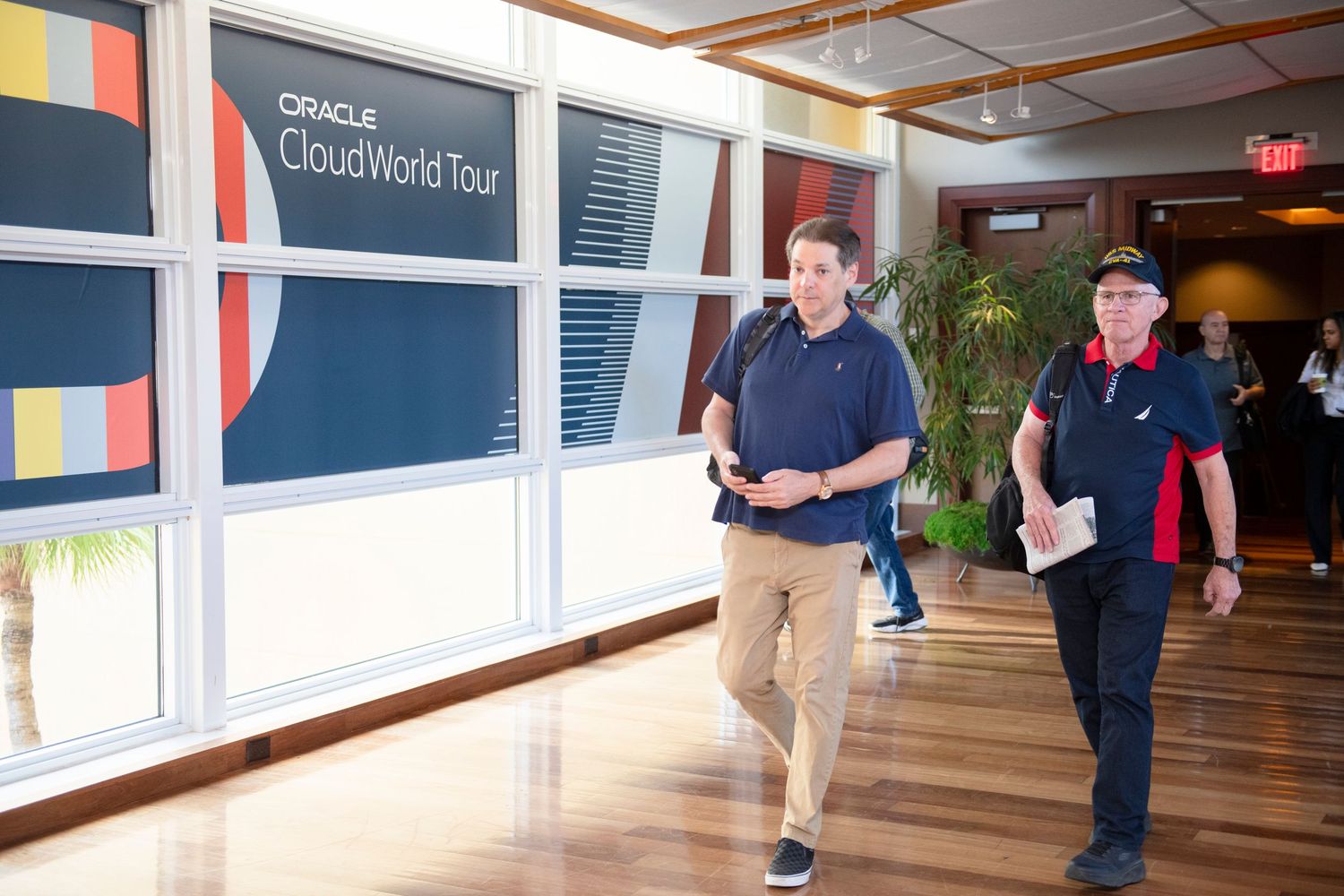 Two professionals walking through Oracle CloudWorld Tour event venue corridor past branded signage.