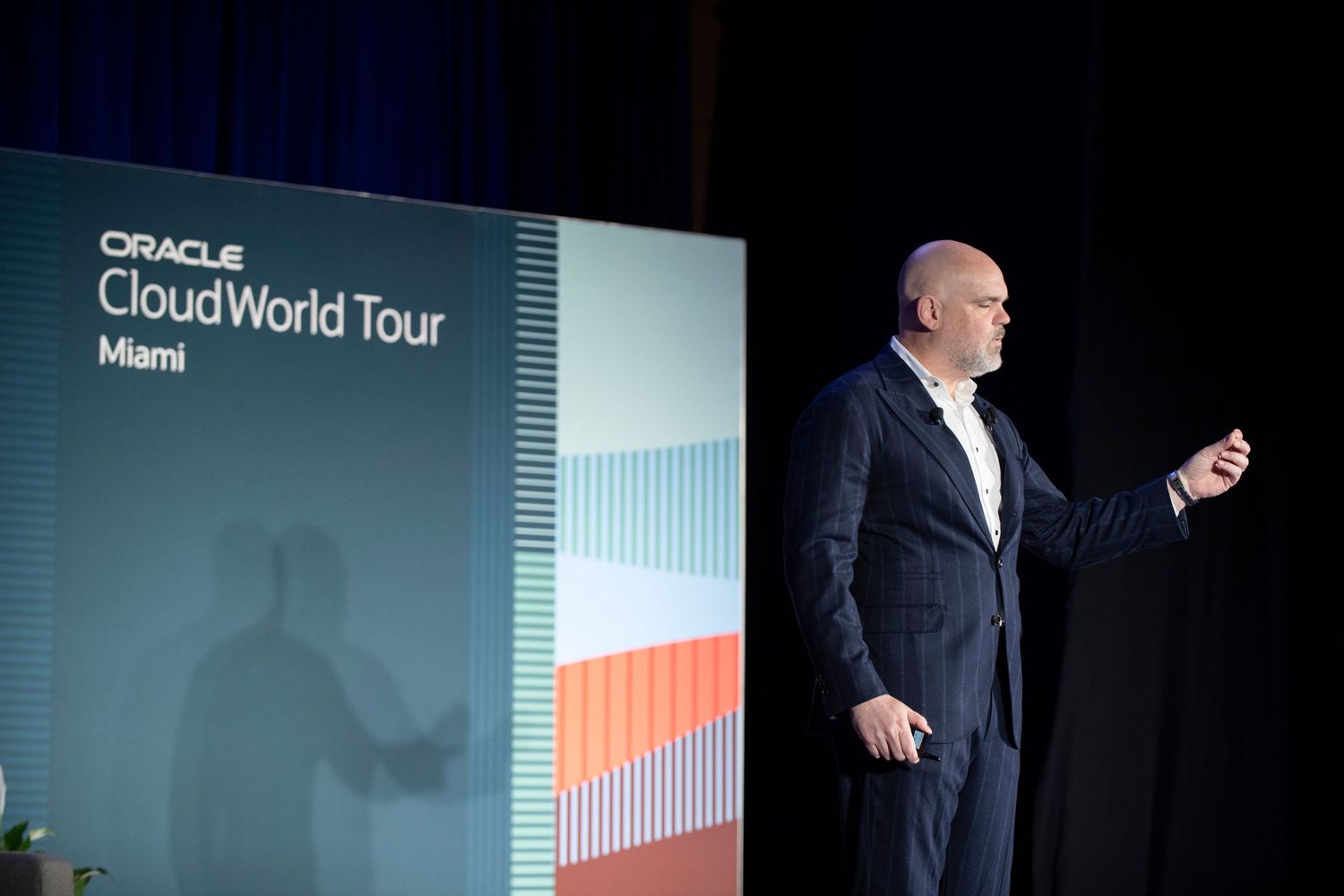Speaker presenting at Oracle CloudWorld Tour Miami event on stage with branded backdrop.