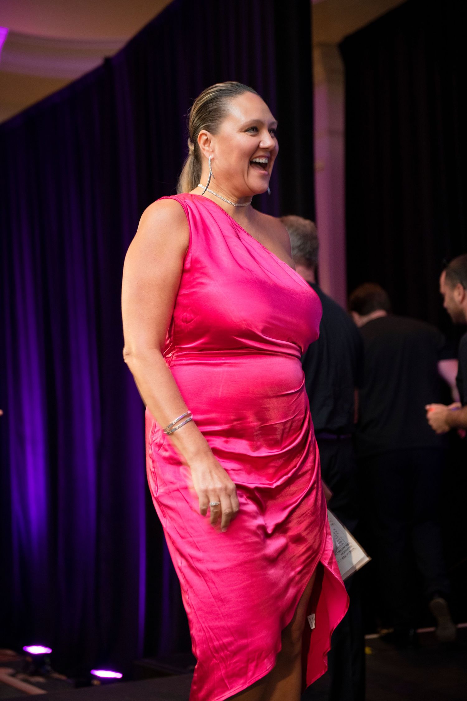 Woman in pink satin one-shoulder dress laughing at formal event.