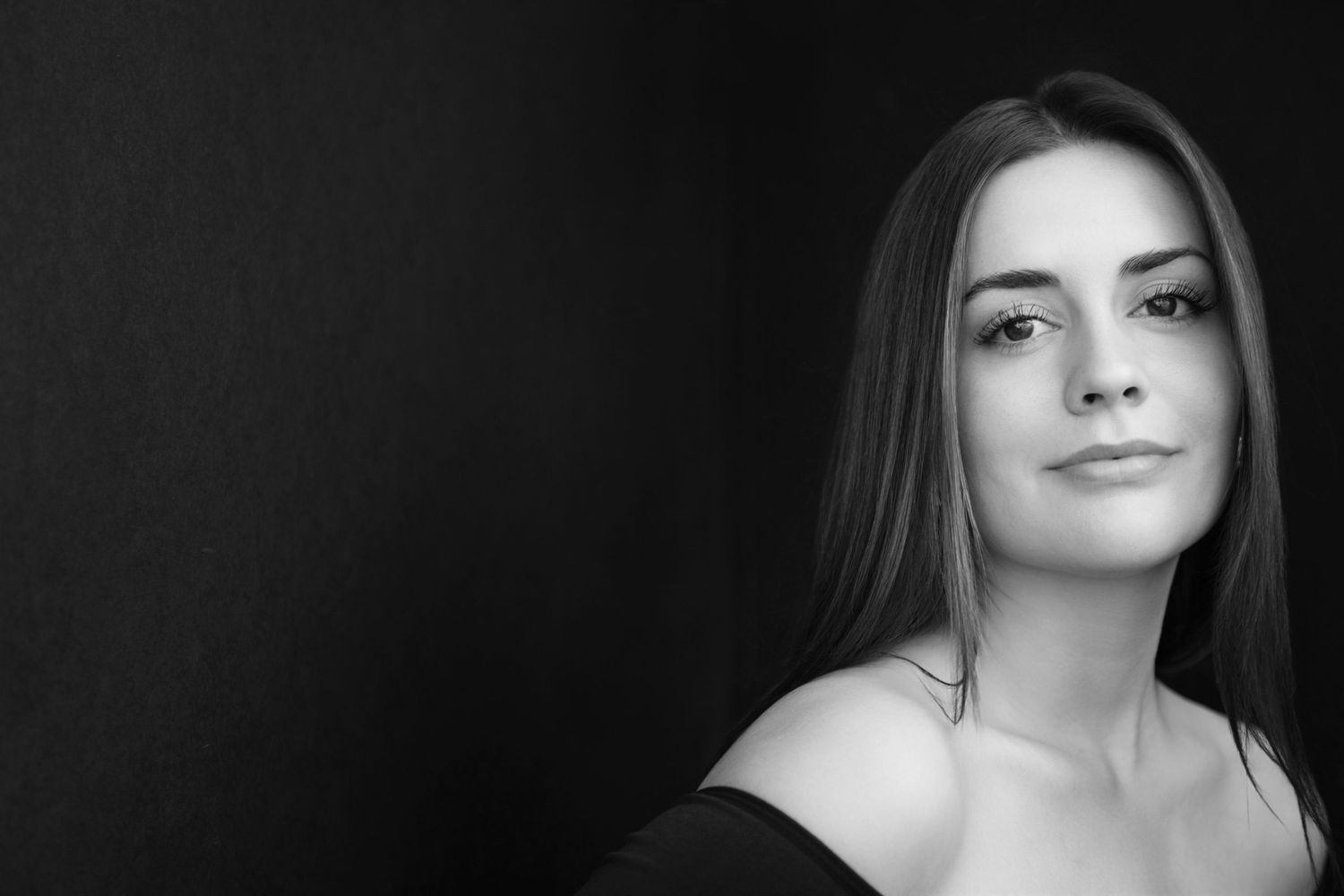 Black and white portrait of a young brunette woman with bare shoulders on dark background.