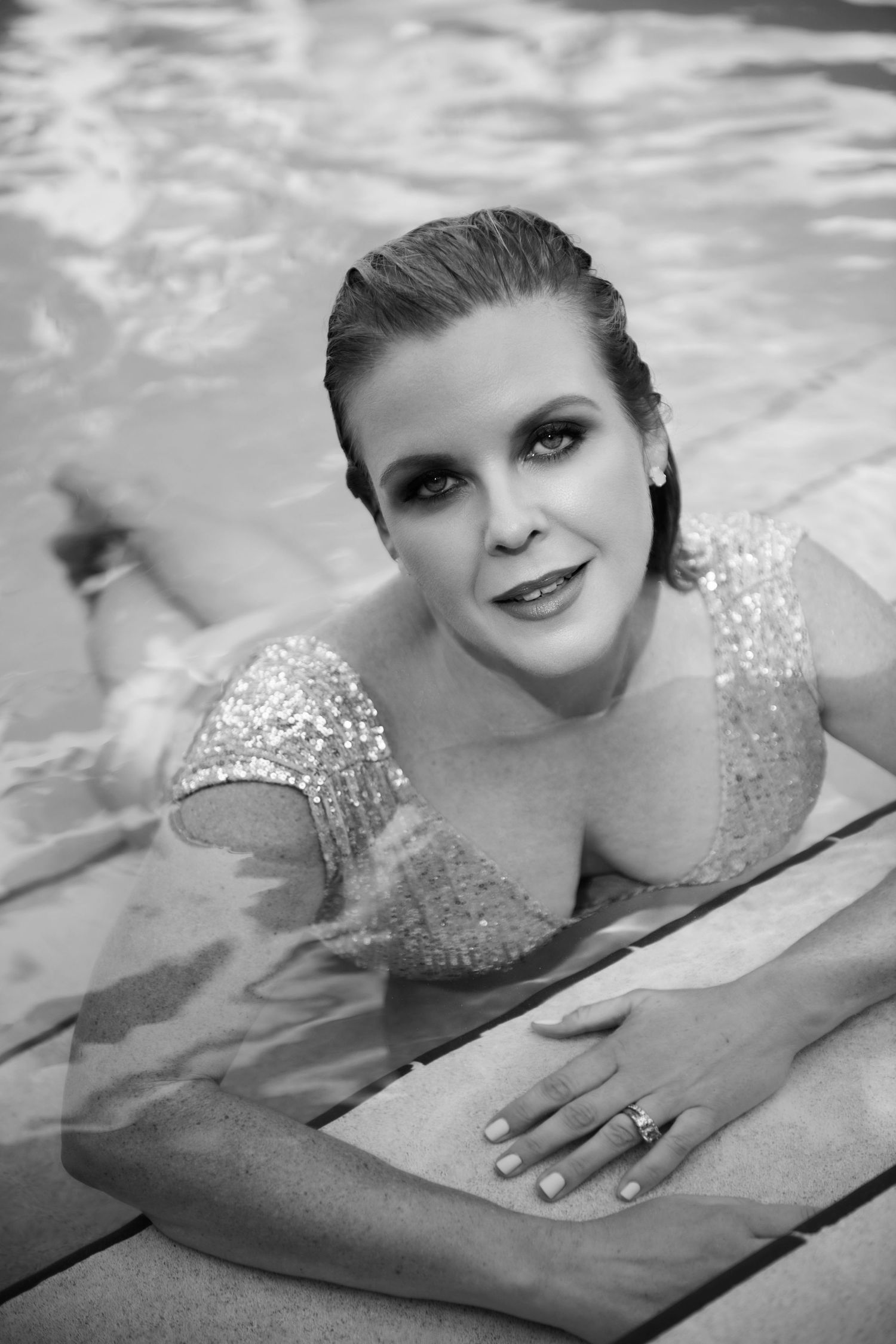 Elegant woman in sequined dress posing at pool edge in glamorous black and white photo.