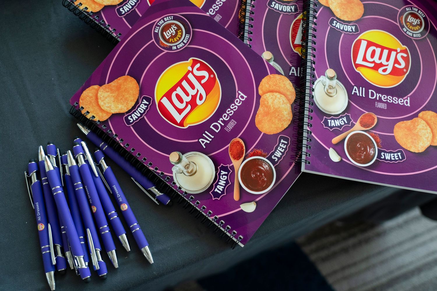 Lay's All Dressed flavor notebooks and blue pens arranged on a dark surface.