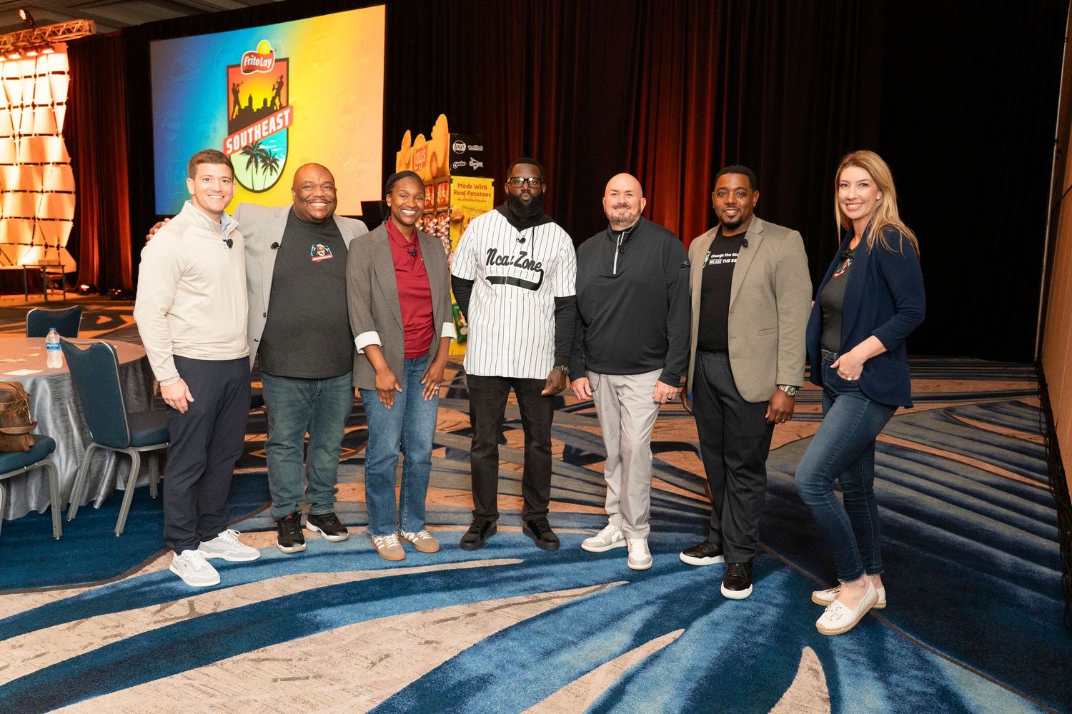 Group of seven people posing together at a conference event in a decorated ballroom venue.